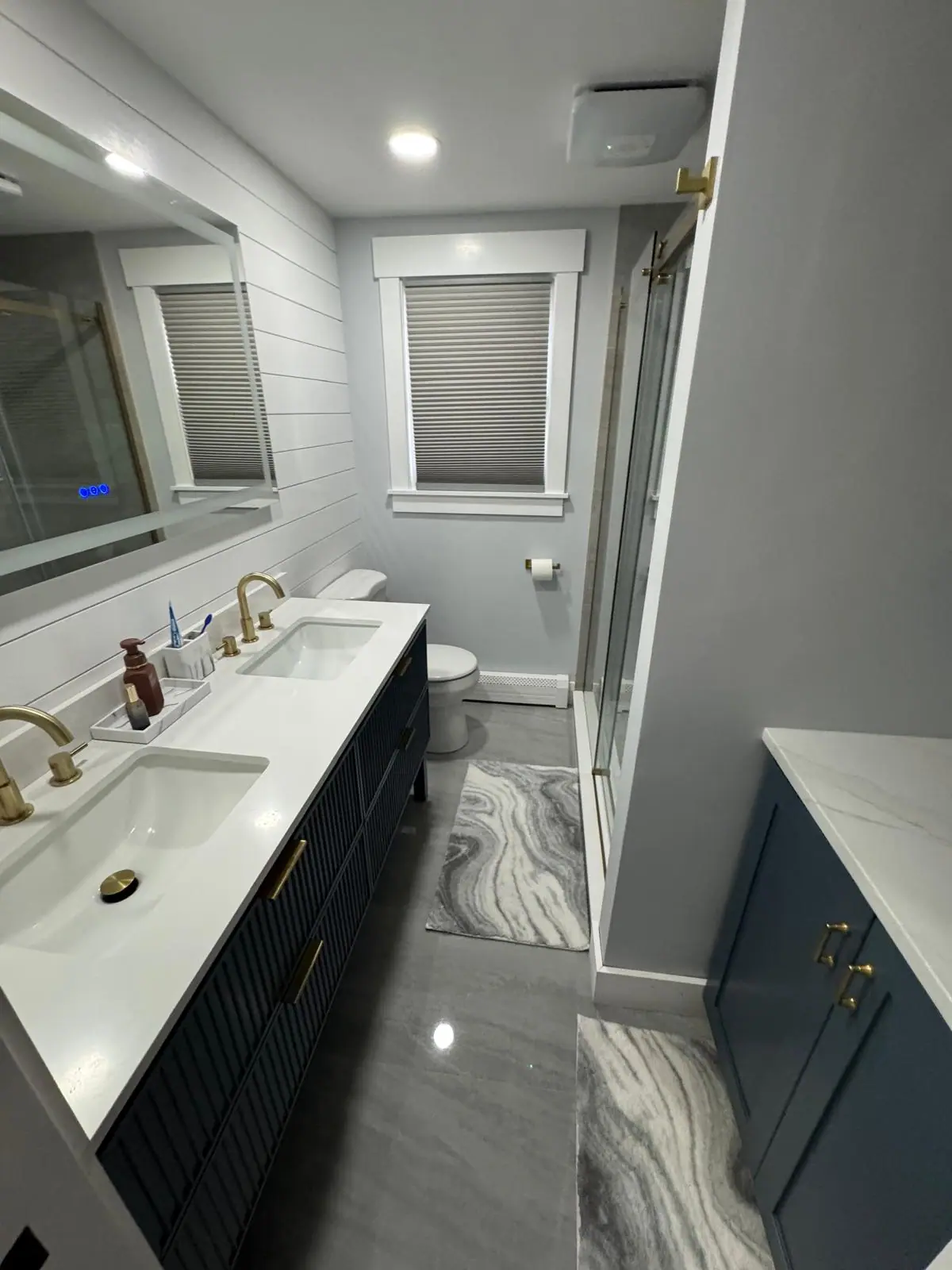 Bathroom with a navy double vanity, gold faucets and a gray tile floor
