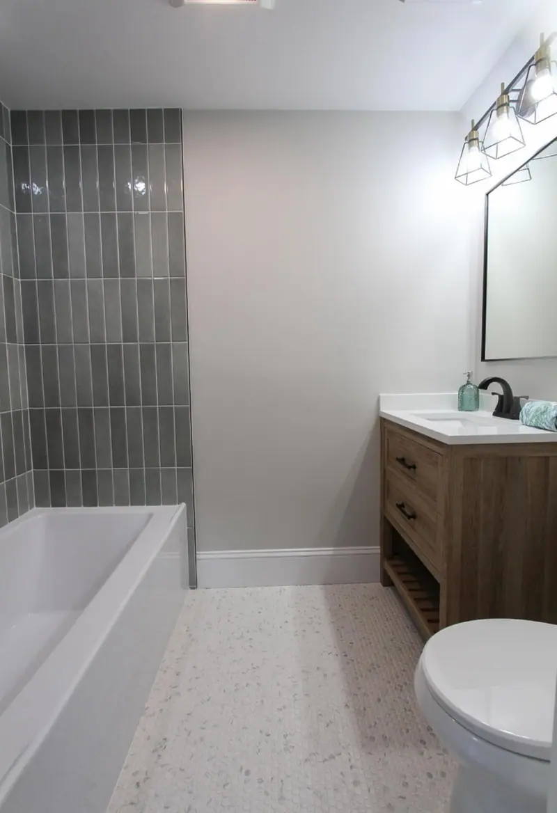 Bathroom with a sage stacked tile tub wall, a wood vanity and a light floor