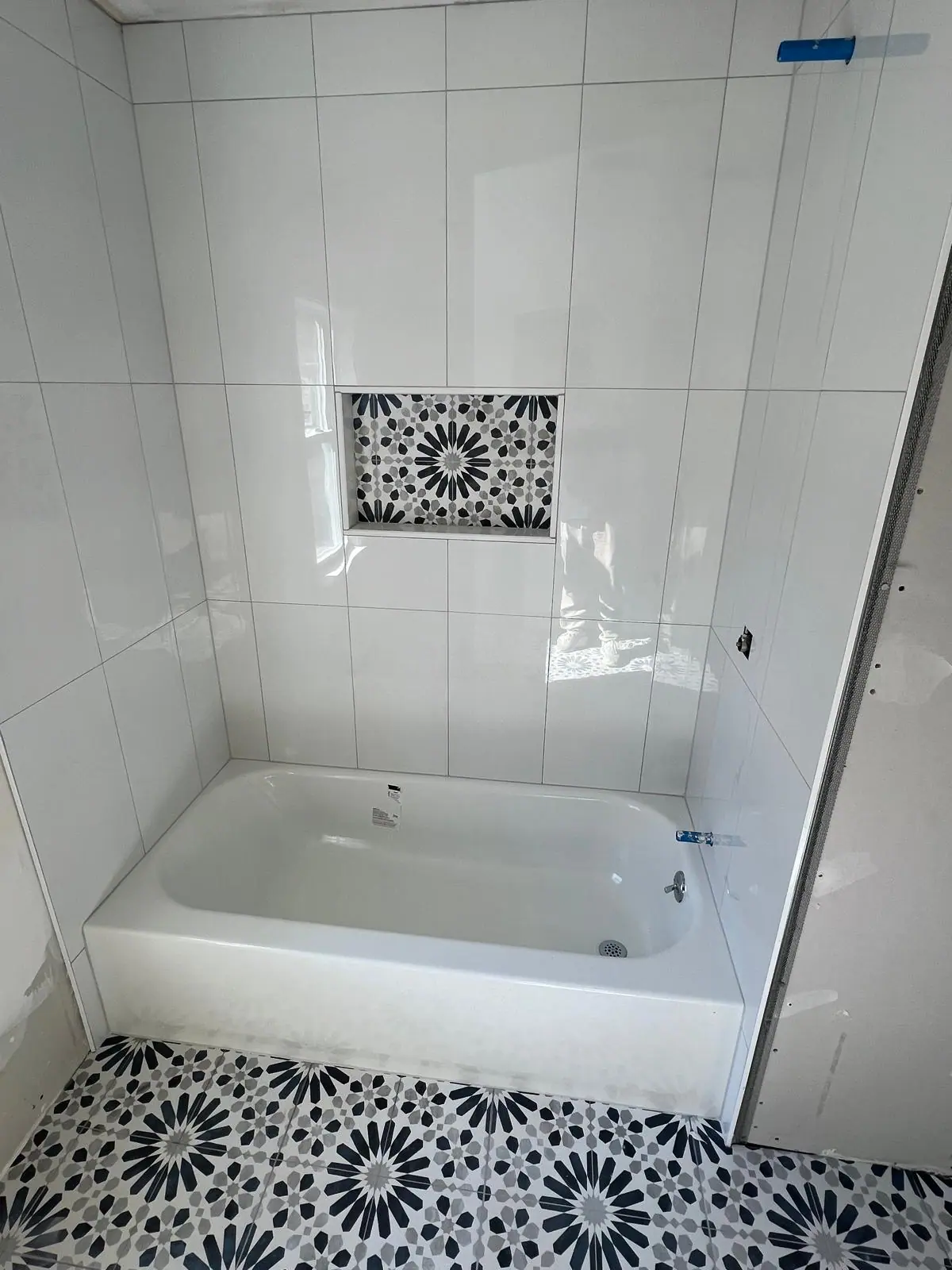 White tub surround with a black and white patterned niche and matching patterned floor tile